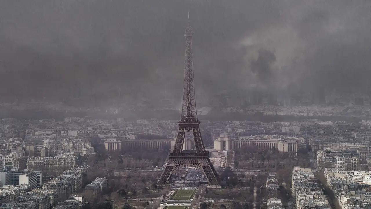 La Torre Eiffel si erge nel centro di Parigi sotto un cielo scuro e nuvoloso, con smog e fumo pesanti che creano un'atmosfera cupa e inquinata sulla città.