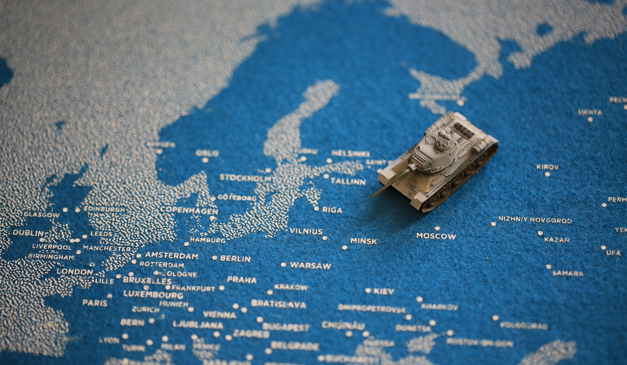 Un carro armato giocattolo si trova su una mappa dettagliata dell'Europa, posizionata vicino a Mosca, con città come Varsavia, Berlino e Copenaghen etichettate intorno. La mappa ha uno sfondo blu con i nomi delle città in bianco.