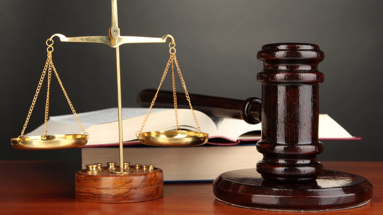 Un martelletto da giudice in legno, una bilancia in ottone e un libro di legge aperto sono appoggiati su una scrivania in legno su uno sfondo scuro, a simboleggiare la giustizia e i procedimenti aperti. In questo caso il riferimento va alle partecipazioni in eredità o donazione: come calcolare l’imposta