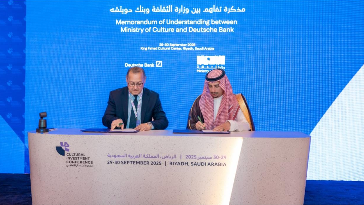 Due uomini seduti a un tavolo firmano dei documenti davanti a uno schermo blu che mostra i dettagli di un memorandum d'intesa tra il Ministero della Cultura e la Deutsche Bank in occasione della 2025 Cultural Investment Conference a Riyadh, in Arabia Saudita.