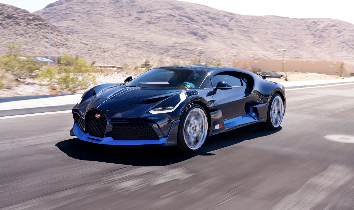 Un'auto sportiva Bugatti nera e blu sfreccia su un'ampia strada in un paesaggio desertico, con montagne e cielo limpido sullo sfondo.