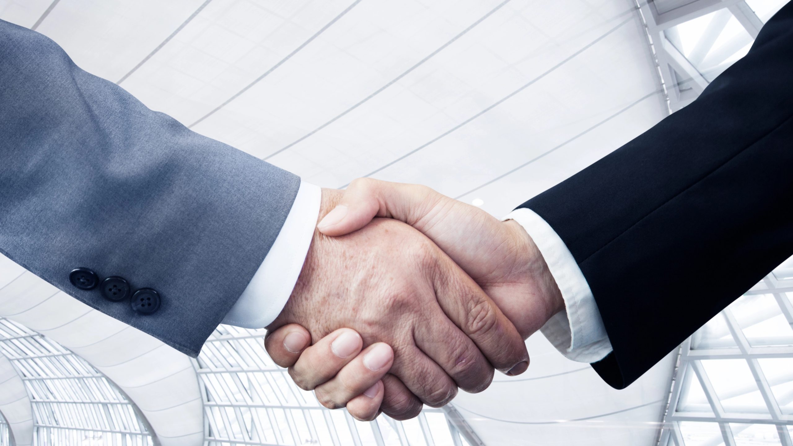 Due persone in abito da lavoro che si stringono la mano, a simboleggiare un accordo o una partnership in un arbitraggio o in un investimento di fondo M&A, con un moderno edificio con soffitto in vetro sullo sfondo.
