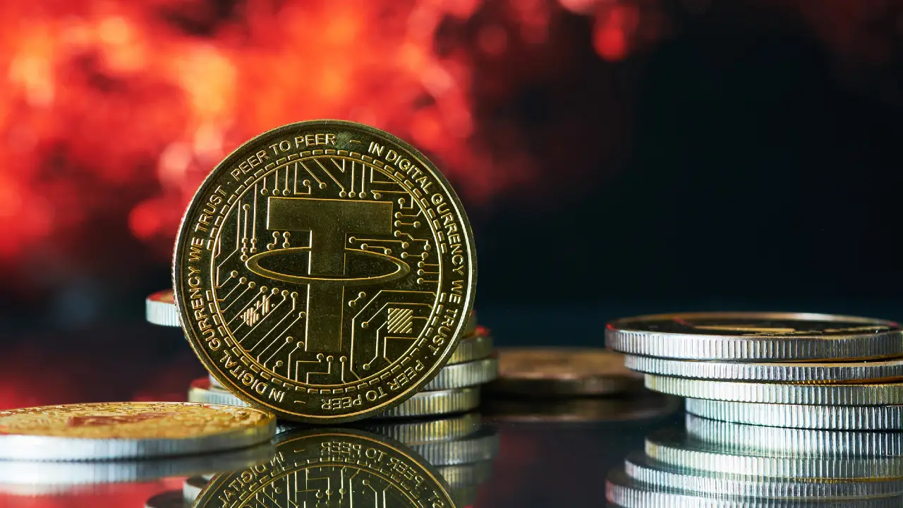 Una moneta d'oro della criptovaluta Tether si trova in piedi tra pile di altre monete su una superficie riflettente, con uno sfondo sfocato rosso fuoco e arancione.