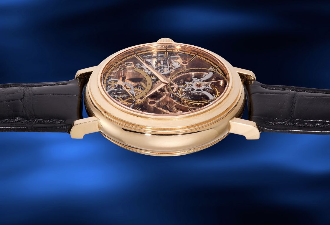 Un orologio da polso d'oro con quadrante scheletrato trasparente, che rivela ingranaggi e meccanismi intricati, è visualizzato su uno sfondo blu sfocato. L'orologio ha un cinturino in pelle nera.