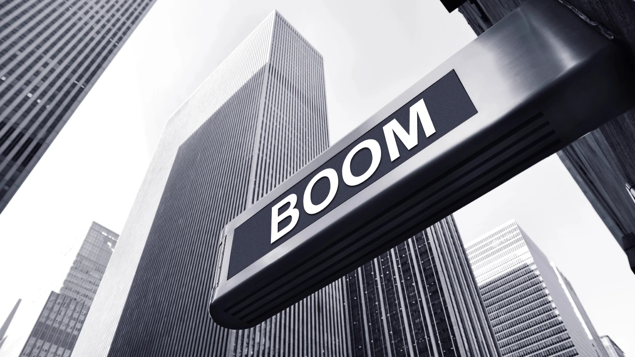 Una grande insegna con la parola "BOOM" in grassetto è mostrata in primo piano, sullo sfondo di alti e moderni grattacieli: un caso eclatante di arte urbana d'impatto. L'immagine è in bianco e nero è fa riferimento alla crescita del mercato delle case in Italia.