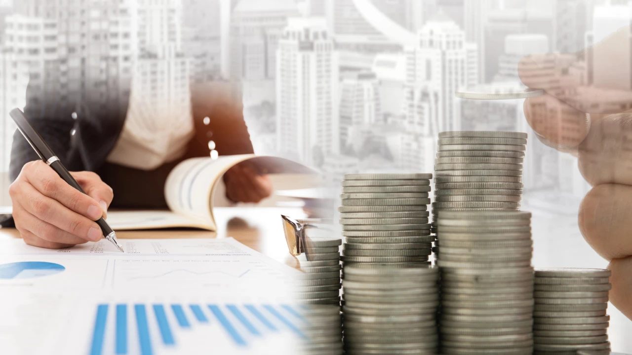 Immagine di una persona che scrive su un taccuino a una scrivania con davanti dei grafici finanziari e pile di monete. Sullo sfondo, degli edifici sfocati di città in riferimento agli investimenti in fondi immobiliari.