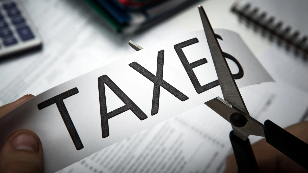 Una persona taglia con le forbici un pezzo di carta con la parola "taxes", che simboleggia la riduzione delle tasse e l’introduzione del ravvedimento speciale con aliquote ridotte e scadenze flessibili per sanare Irpef, Iva e imposte arretrate.