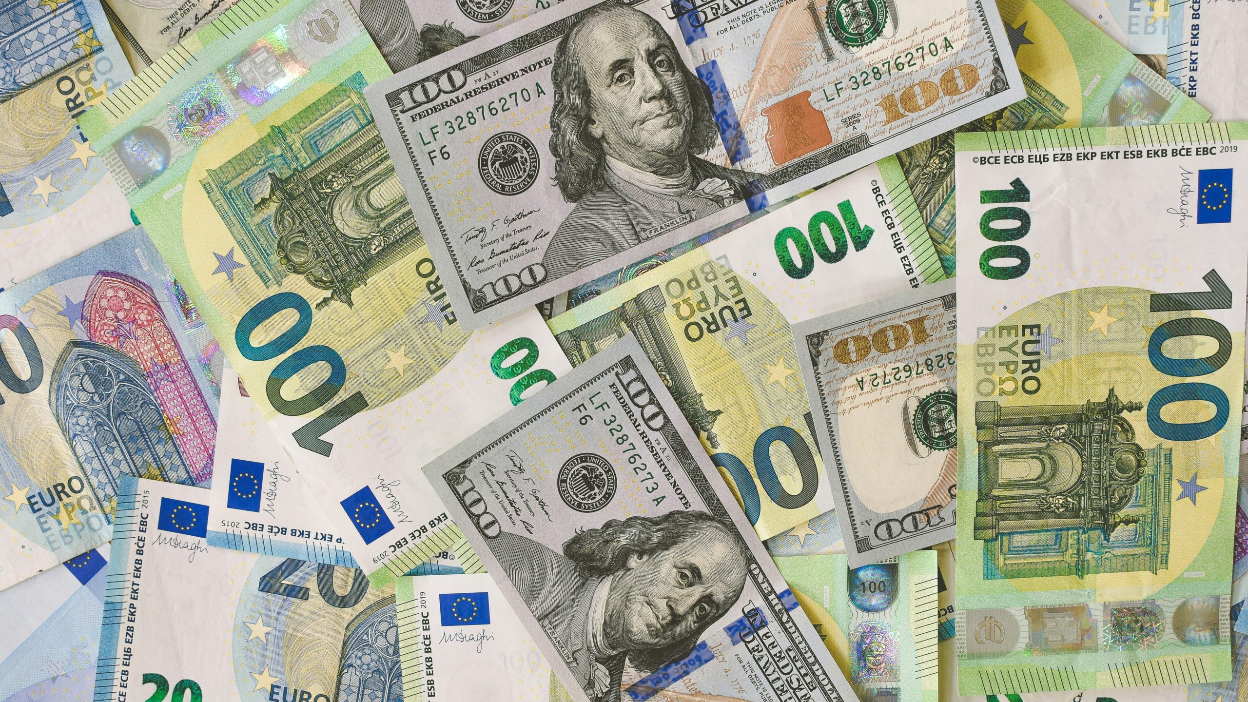 Un mucchio sparso di banconote da 100 dollari USA e 100 euro, che mostra entrambe le valute in primo piano con dettagli e colori visibili.