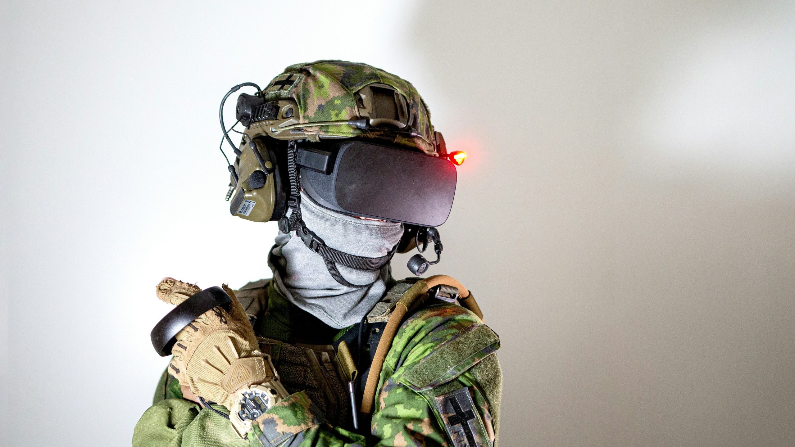 Una persona in tenuta mimetica militare e guanti, che rappresenta il collegamento a investire in fondi ed Etf sulla difesa, indossa una cuffia per la realtà virtuale con una luce rossa, cuffie e microfono, su uno sfondo bianco.