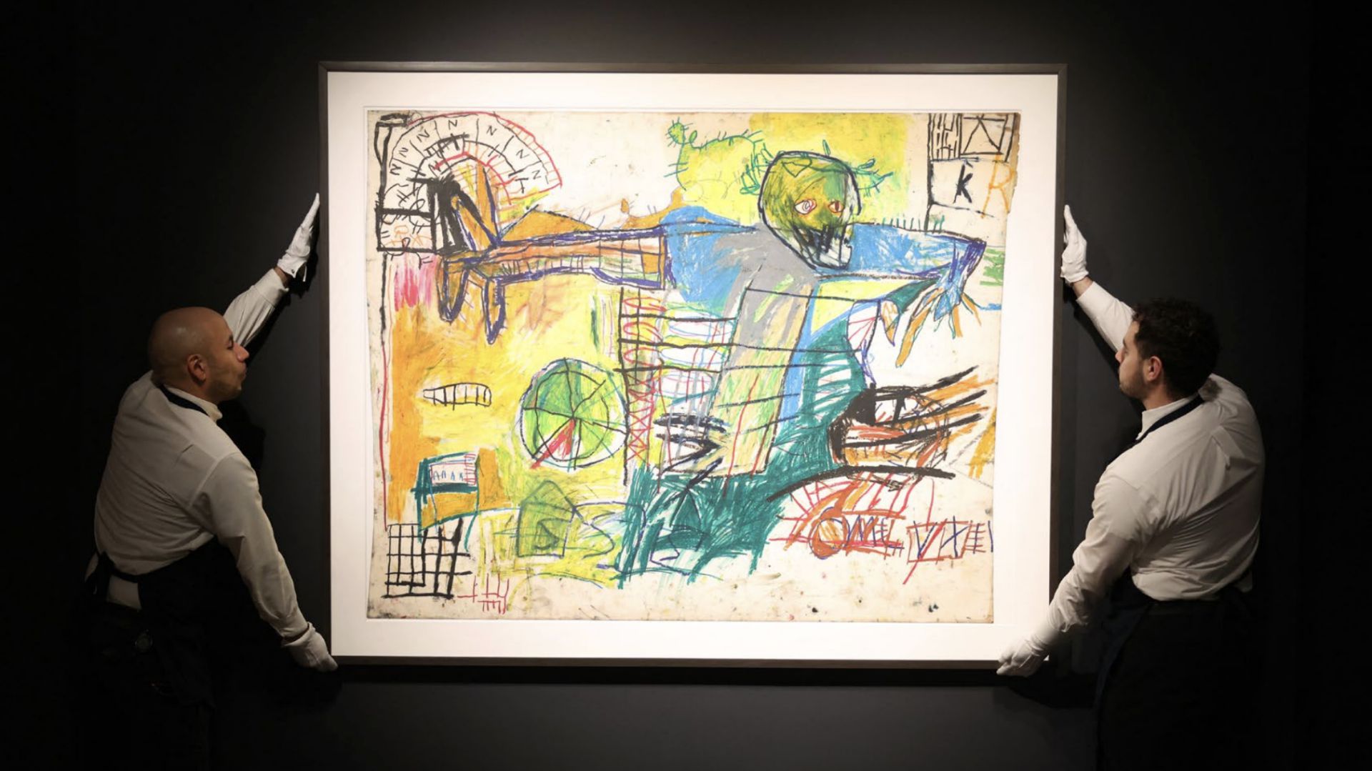 Due addetti all'arte che indossano guanti bianchi posizionano un dipinto astratto incorniciato con colori vivaci e linee caotiche su una parete scura. L'opera raffigura una figura umana distorta e varie forme geometriche.