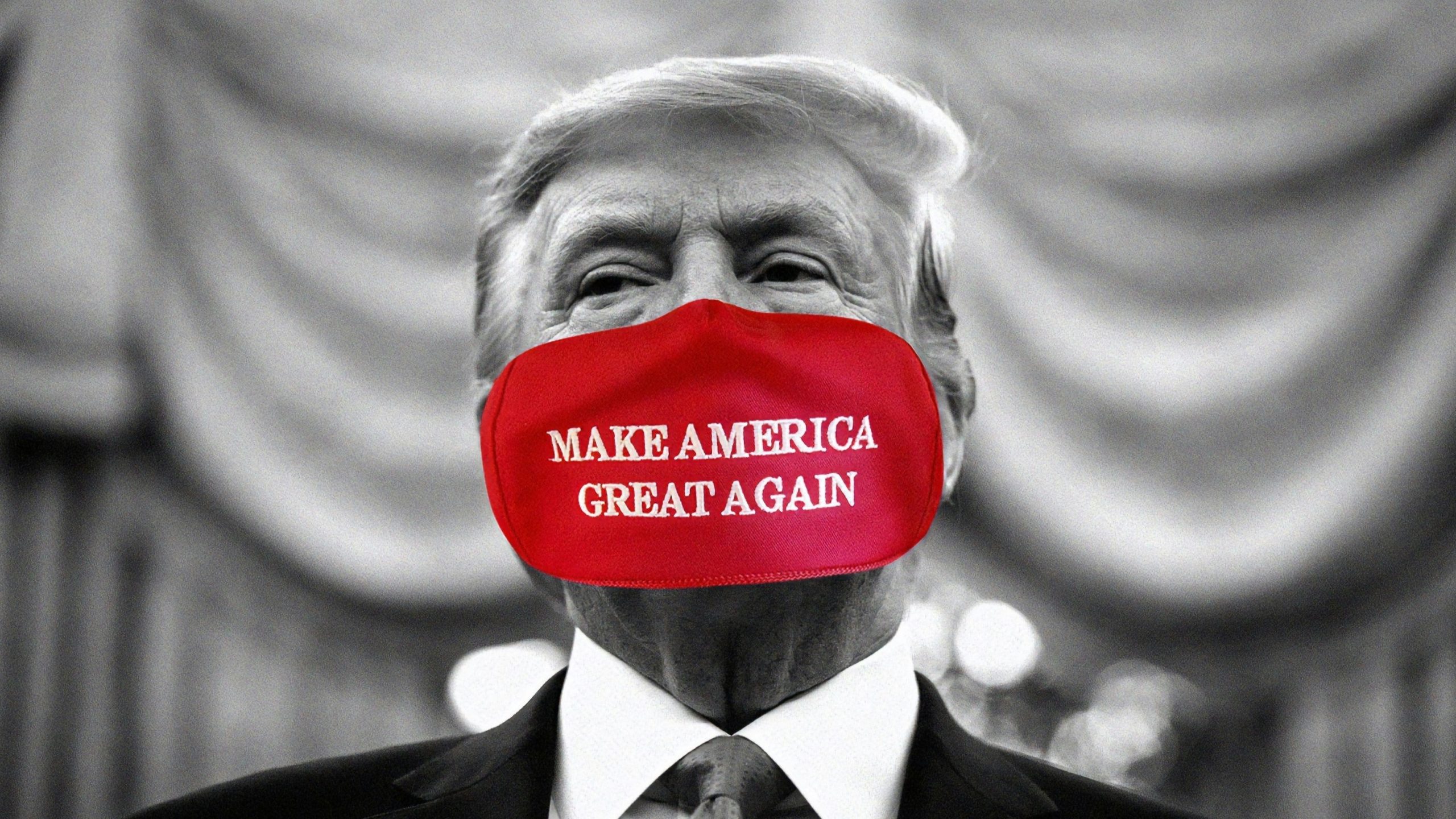Un uomo in giacca e cravatta indossa una maschera rossa con la scritta "MAKE AMERICA GREAT AGAIN". L'immagine è in bianco e nero, tranne la maschera che è a colori.