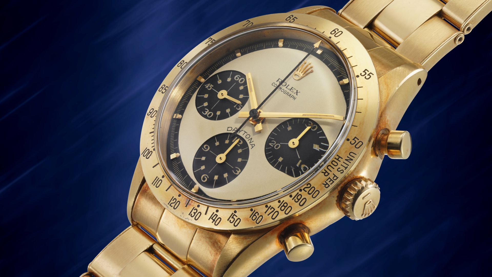 Un primo piano di un orologio Rolex Daytona in oro con quadrante champagne, contatori neri e lunetta tachimetrica, su sfondo blu: un'icona spesso presente in aste prestigiose come asta 10 anni Phillips.