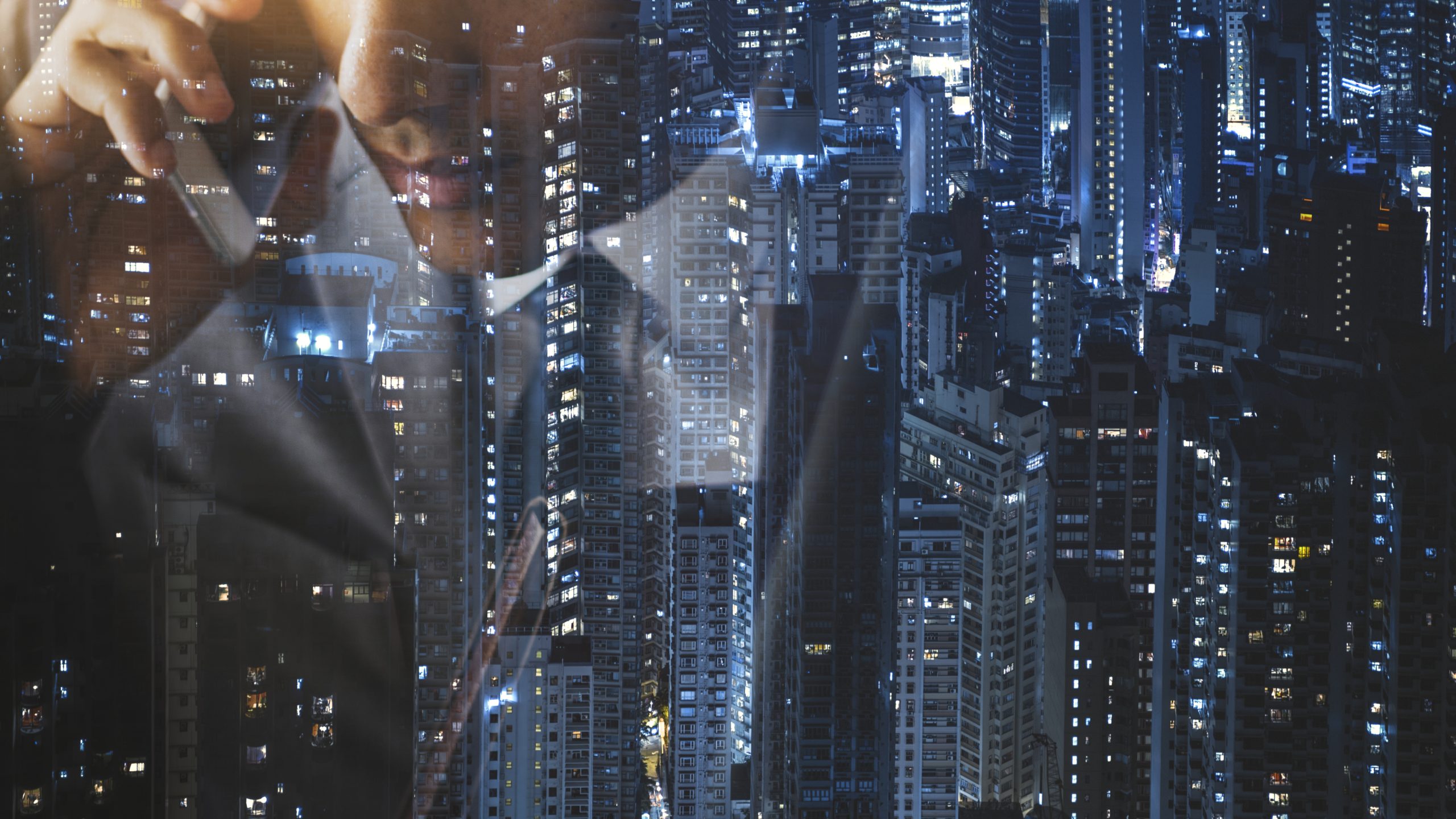 Un uomo in giacca e cravatta, visto in un primo piano parziale, sta parlando al telefono. La sua immagine si fonde con lo skyline della città di notte, a simboleggiare il mondo dinamico di Weltix infrastruttura fintech e dei beni privati.