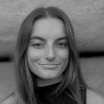 Ritratto in bianco e nero di Emilia Taddonio, giovane donna con capelli lunghi e lisci, che indossa un top senza maniche e guarda direttamente verso la macchina fotografica con un leggero sorriso e uno sfondo neutro.