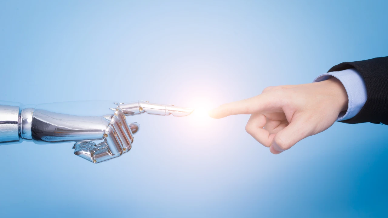 Una mano umana e una mano robotica si protendono l'una verso l'altra, con gli indici che quasi si toccano e una luce di rete incandescente nel punto di contatto, su uno sfondo blu.