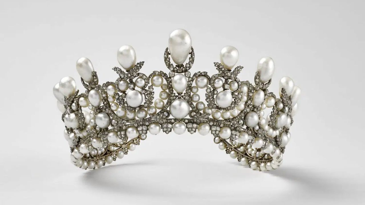 Un diadema lussuoso, che ricorda i tesori perduti nel furto gioielli del Louvre, ornato da perle grandi e piccole in motivi elaborati e diamanti scintillanti, incastonati in argento o platino su uno sfondo chiaro.