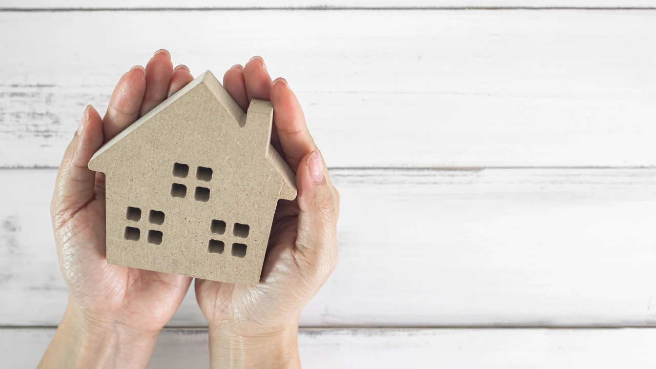Due mani tengono delicatamente un piccolo modello di casa in cartone con finestre ritagliate, simbolo che la casa è un bene rifugio per gli italiani.
