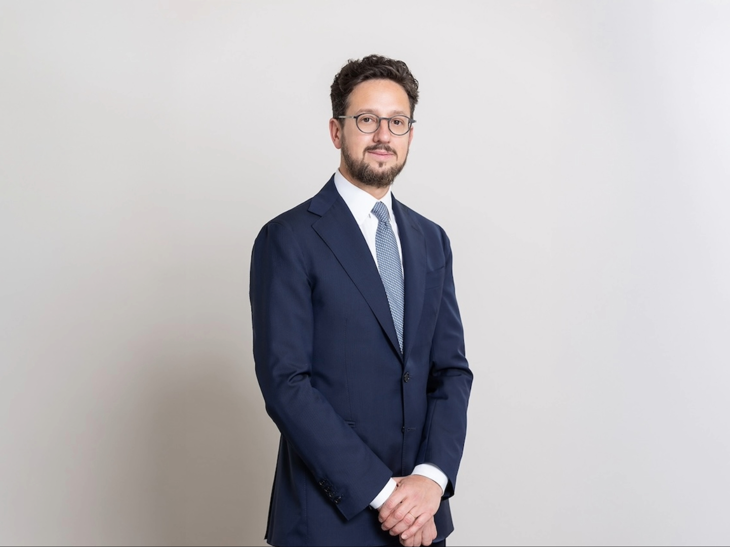 Un uomo in abito blu scuro, cravatta azzurra e occhiali si staglia su un semplice sfondo chiaro, incarnando la qualità degli investimenti che Banor apprezza, mentre guarda l'obiettivo con un'espressione neutra e le mani sciolte.