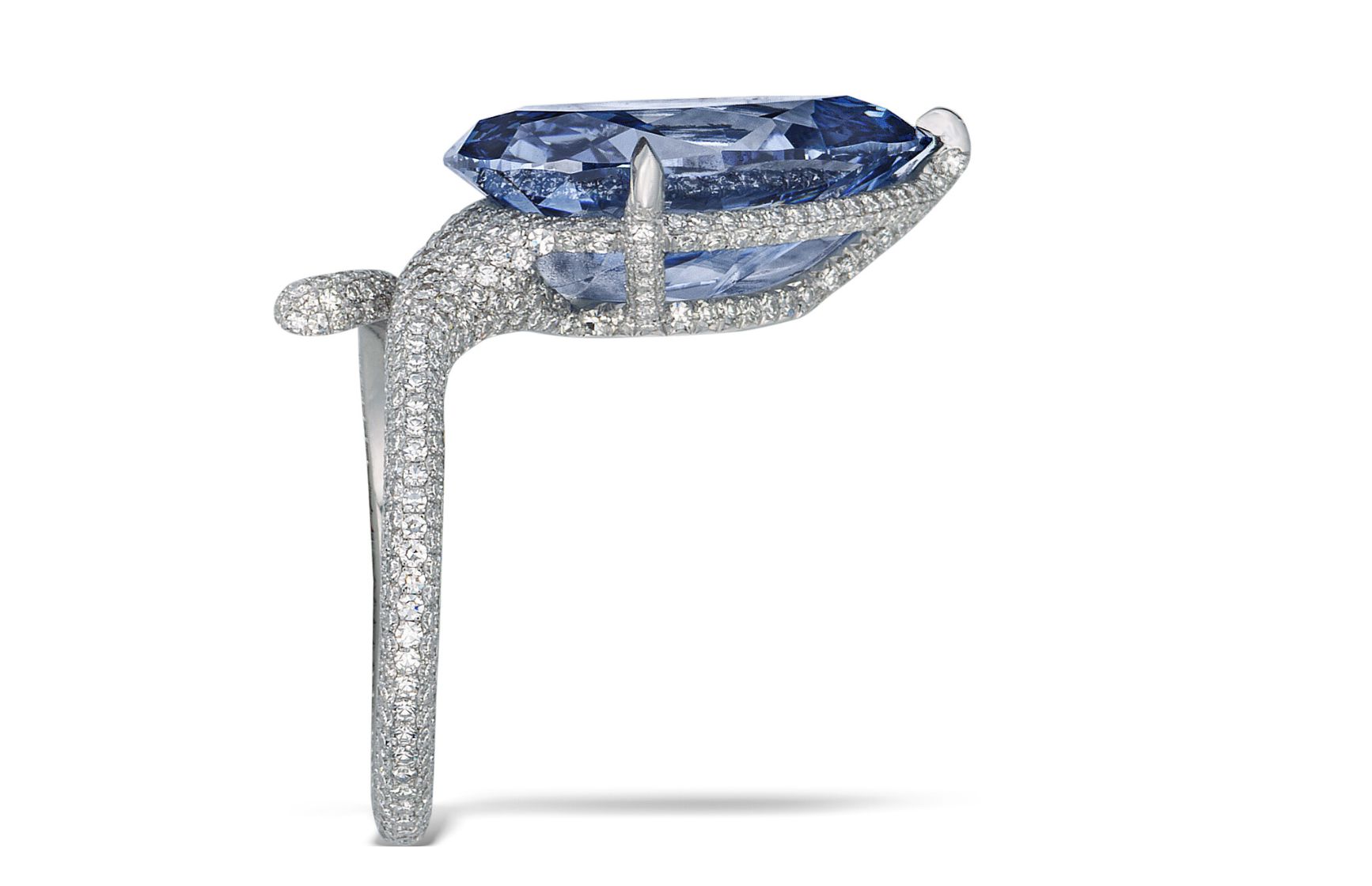 Vista laterale di un elegante anello con una grande gemma blu di taglio ovale sostenuta da quattro griffe, incastonata su una fascia di metallo bianco con piccoli diamanti bianchi.