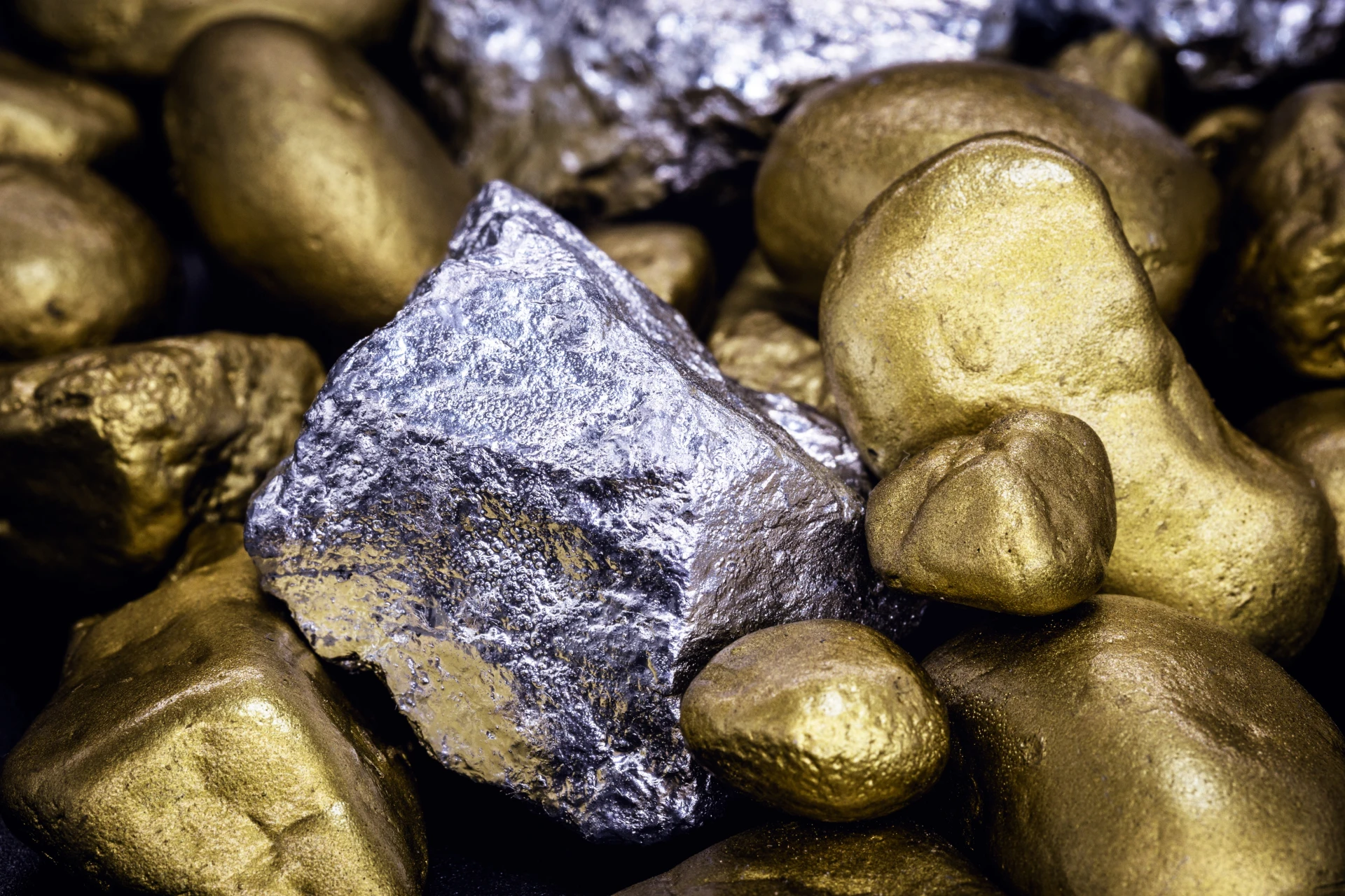 Primo piano di diverse pepite metalliche d'oro e d'argento lucide con superfici ruvide e irregolari, raggruppate a stretto contatto. La pepita d'argento è al centro, circondata da pepite d'oro.