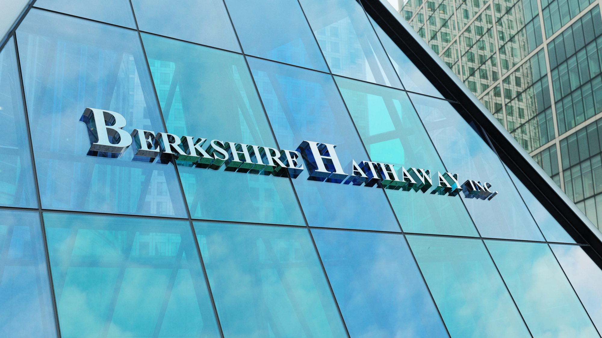 Una facciata in vetro che riflette i grattacieli vicini, con grandi lettere metalliche che scrivono "Berkshire Hathaway Inc." affisse all'esterno.