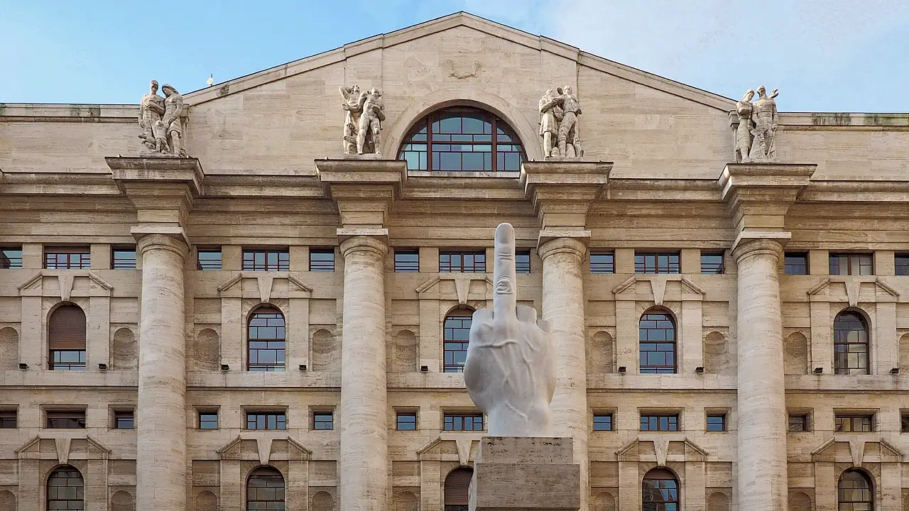 Un grande edificio in pietra con colonne e statue sul tetto, in cui spicca la scultura bianca di una mano con il dito medio alzato in primo piano.