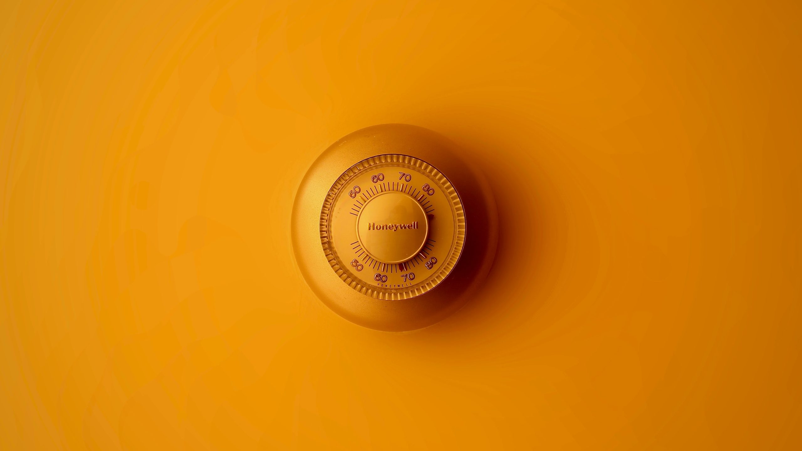 Il quadrante di una serratura o di una cassaforte a combinazione rotonda e metallica, con la scritta "Honeywell", è centrato su uno sfondo arancione. I numeri e le marcature sul quadrante sono chiaramente visibili.