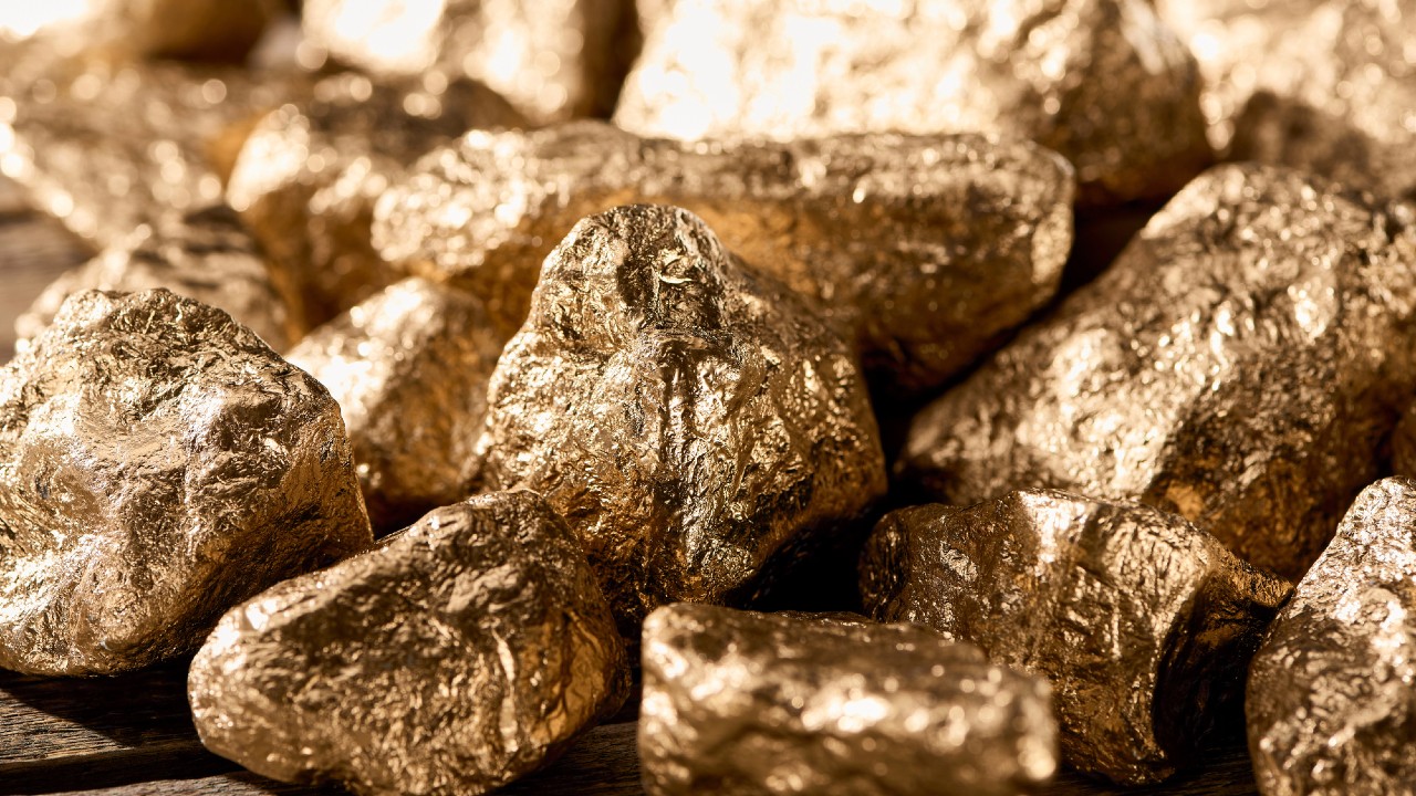 A close-up view of several shiny, rough gold nuggets clustered together on a surface, highlighting their textured surfaces and metallic luster.