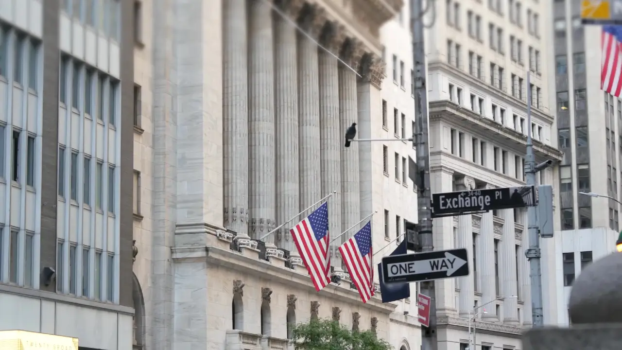Una scena di strada cittadina mostra l'edificio della Borsa di New York con bandiere americane, alte colonne e i vicini cartelli stradali di Exchange Place e One Way. I dintorni sono caratterizzati da una classica architettura in pietra.