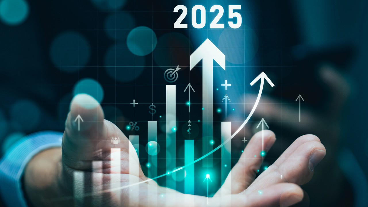 La mano di una persona è tesa con grafici digitali che mostrano frecce verso l'alto, grafici a barre e icone che rappresentano la crescita. L'anno "2025" è visualizzato sopra, a simboleggiare il futuro progresso economico o finanziario.
