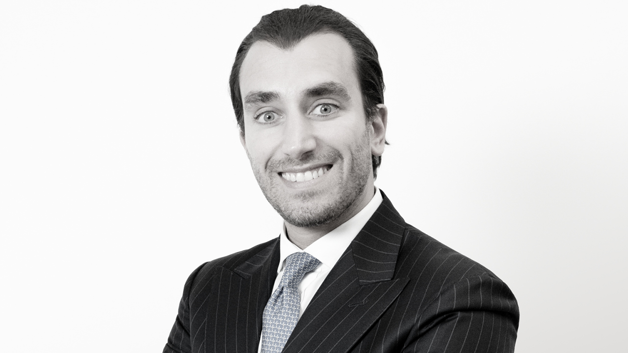 Alessandro Verdirrame di Ares Wealth Management in abito gessato scuro e cravatta chiara sorride alla telecamera con le braccia incrociate, rappresentando Ares mercati privati, su uno sfondo bianco.