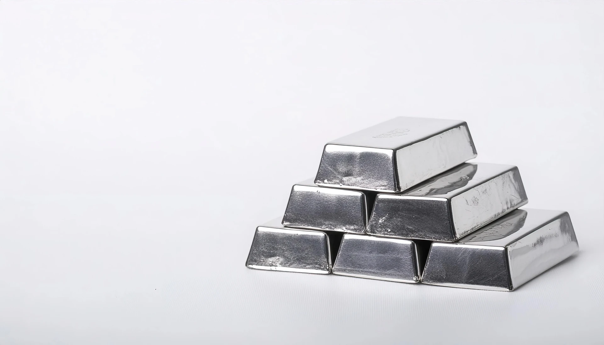 Sei lingotti d'argento lucido, ideali per gli investimenti in argento, sono impilati a piramide su un semplice sfondo bianco, con tre lingotti in basso, due al centro e uno in alto.