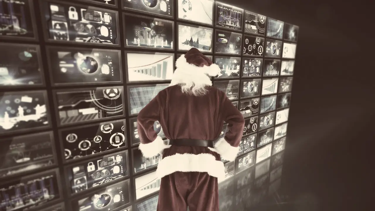 Una persona vestita da Babbo Natale sta in piedi con le mani sui fianchi, di fronte a una grande parete di schermi che mostrano vari grafici digitali, diagrammi e analisi dei dati.