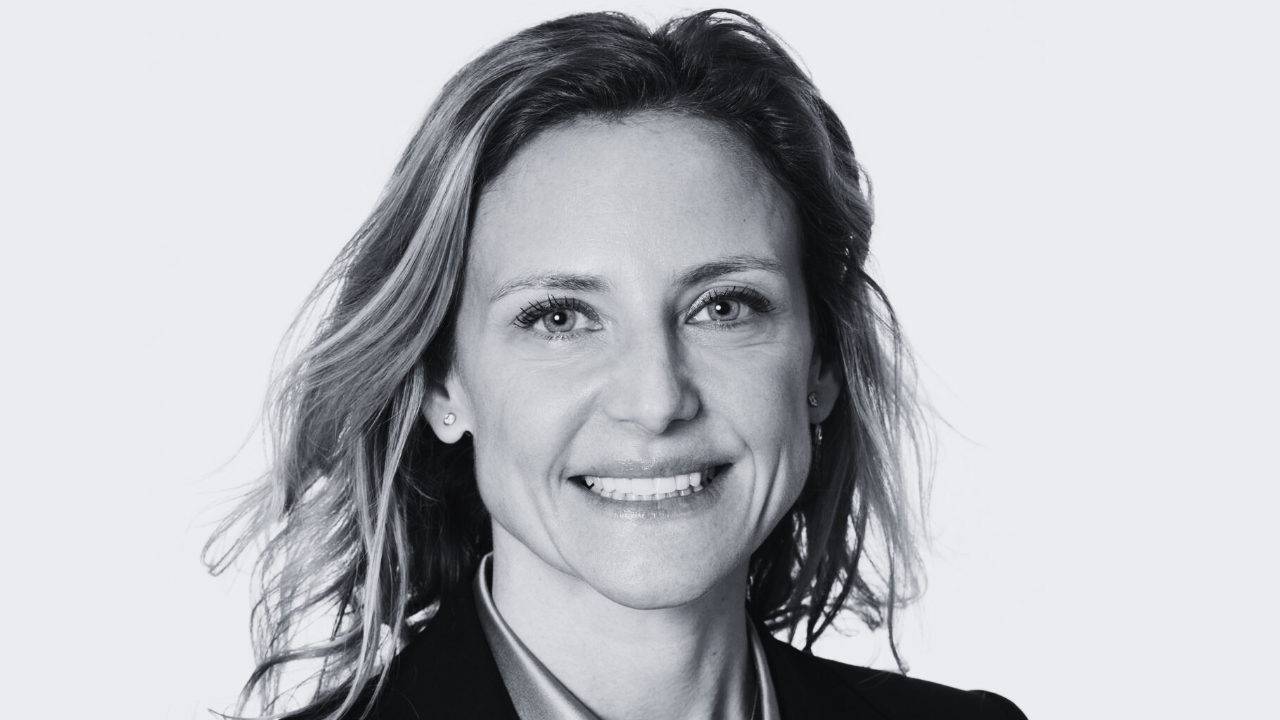 Ritratto in bianco e nero di una donna sorridente con capelli ondulati, che indossa un blazer e una camicia con colletto, rivolta verso l'obiettivo su uno sfondo semplice: un'immagine di ispirazione per chi vuole investire nel 2026.