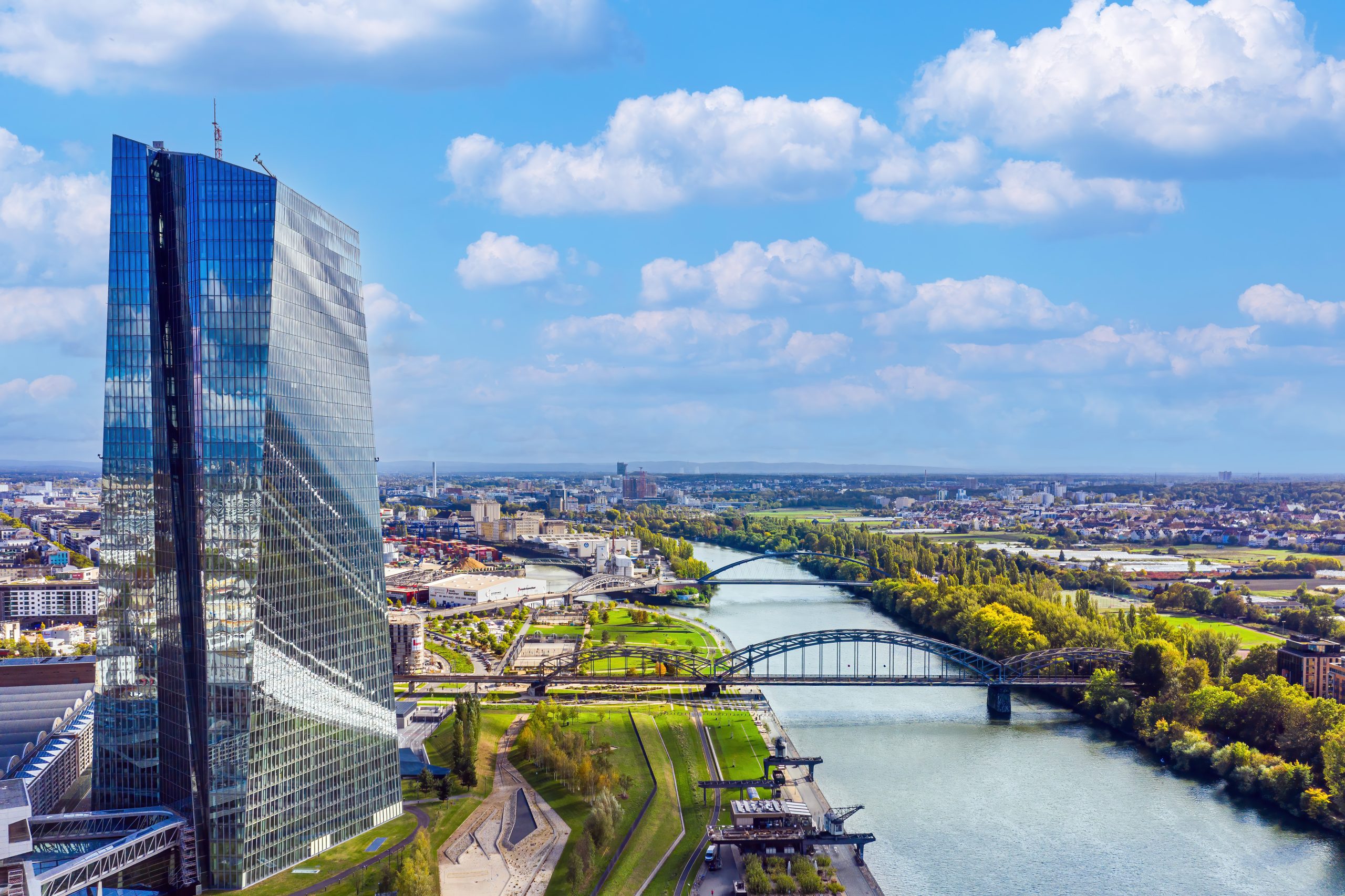 Veduta aerea della sede della BCE a Francoforte affacciata sul fiume Meno, con la città e le infrastrutture finanziarie circostanti.