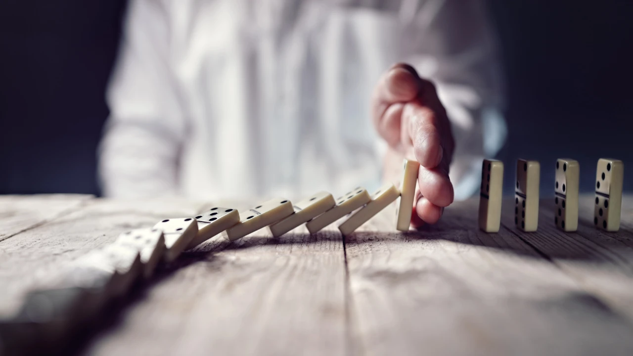 Mano che ferma una catena di tessere del domino per bloccare un effetto a catena finanziario, simbolo del rallentamento dei pagamenti bancari