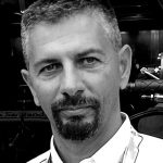 Black and white portrait of a man with short hair, a goatee, and mustache, wearing a collared shirt and a lanyard. He is looking at the camera with a neutral expression.