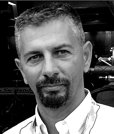 Black and white portrait of a man with short hair, a goatee, and mustache, wearing a collared shirt and a lanyard. He is looking at the camera with a neutral expression.