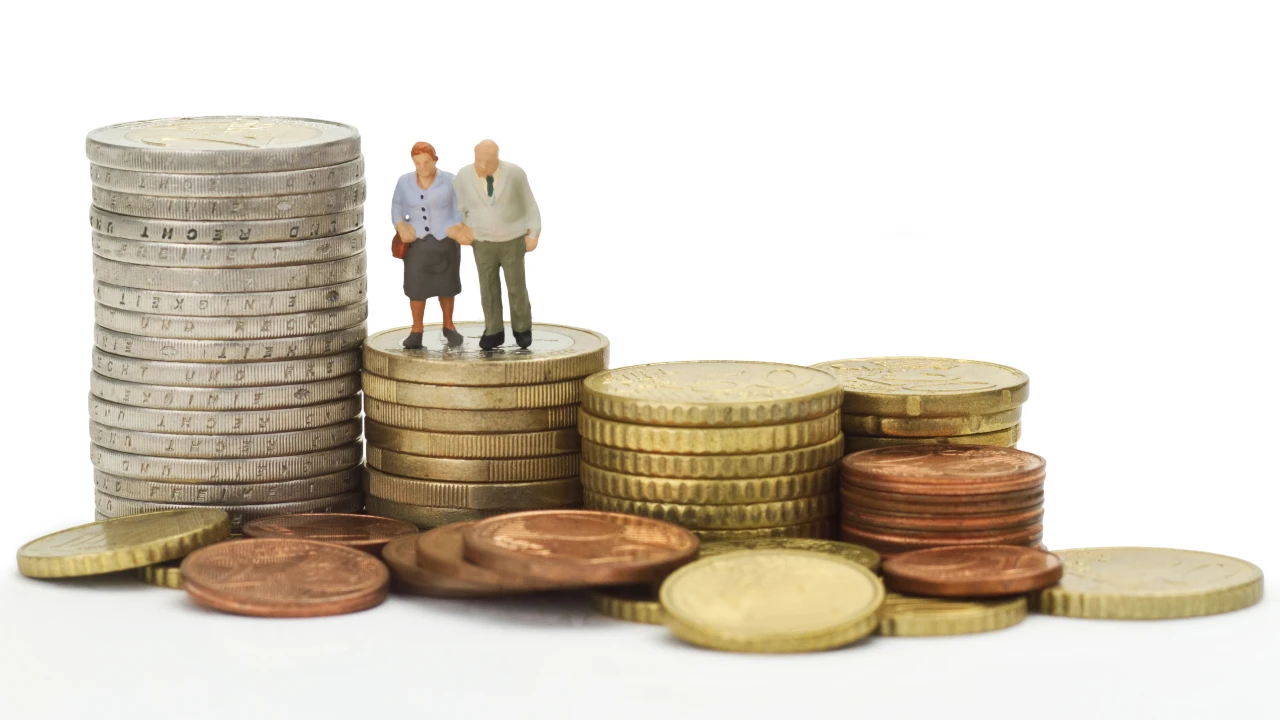 Una coppia di anziani in miniatura si trova su una pila di monete, circondata da vari mucchietti di monete, che simboleggiano il risparmio pensionistico di enasarco e la pianificazione finanziaria per la vecchiaia.