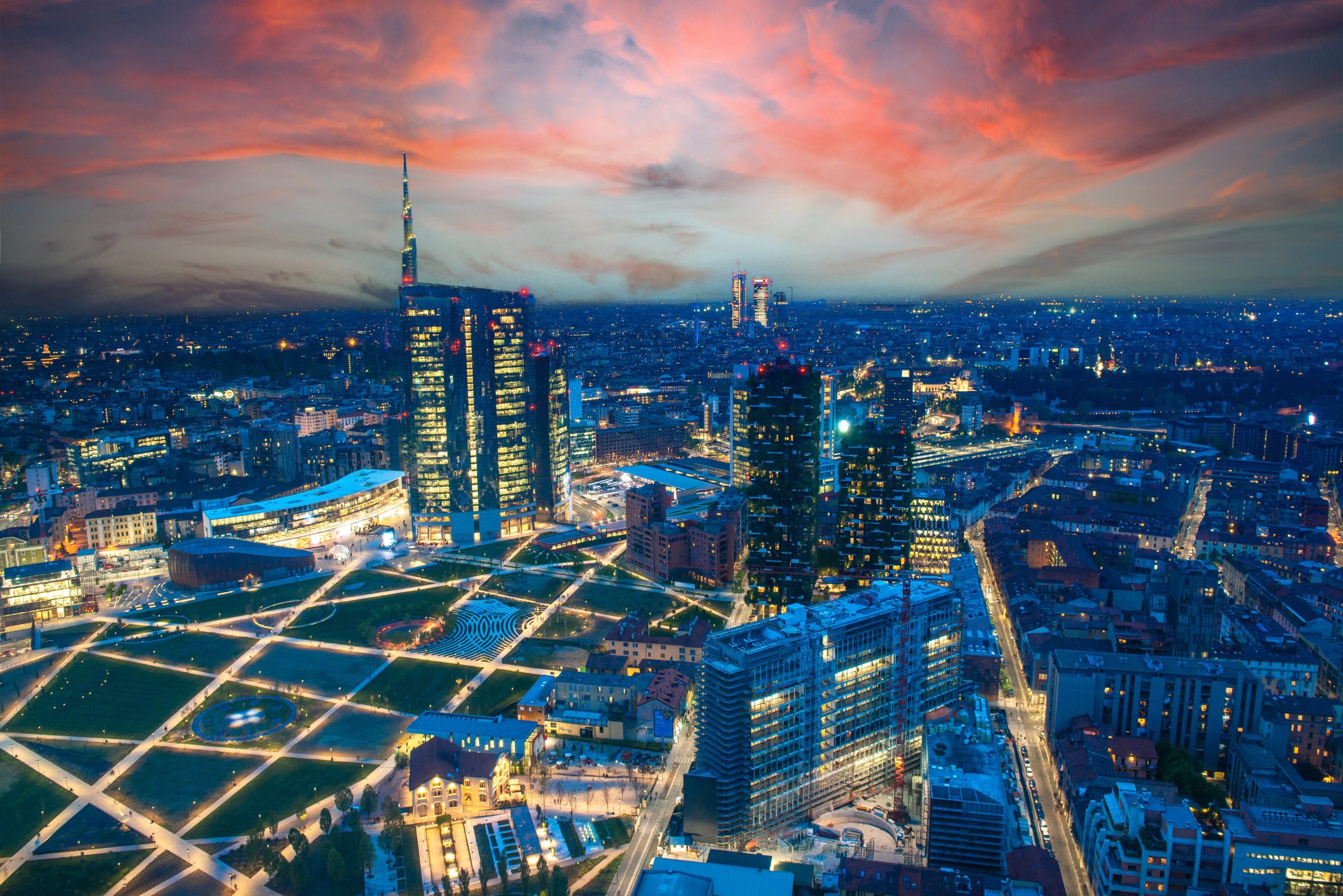 Skyline finanziario di Milano al tramonto con Porta Nuova e Torre UniCredit illuminate.