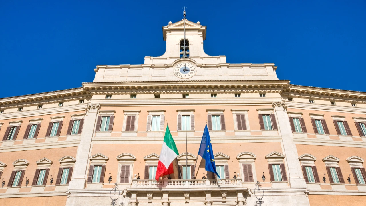 Facciata di Palazzo Montecitorio con bandiere italiana ed europea, simbolo della stabilità fiscale dell’Italia nel 2026.