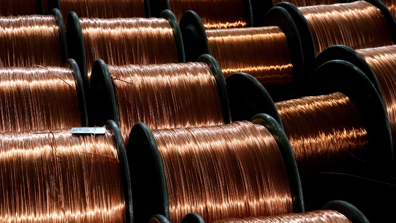 Grandi bobine di filo di rame lucido sono ordinatamente allineate in file, riflettendo la luce e creando una lucentezza metallica. I fili di rame strettamente avvolti sono organizzati per uso industriale o manifatturiero.