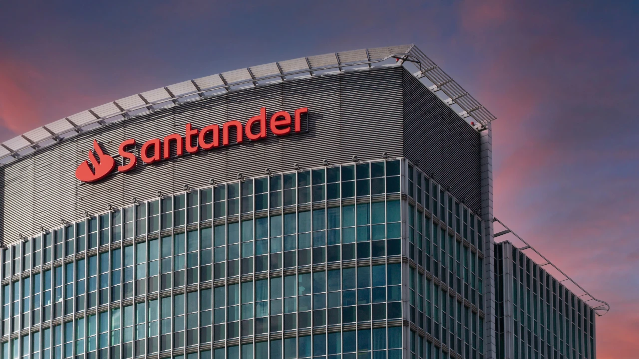 Facciata del quartier generale di Banco Santander al tramonto, con il logo rosso ben visibile sulla sommità dell’edificio in vetro.