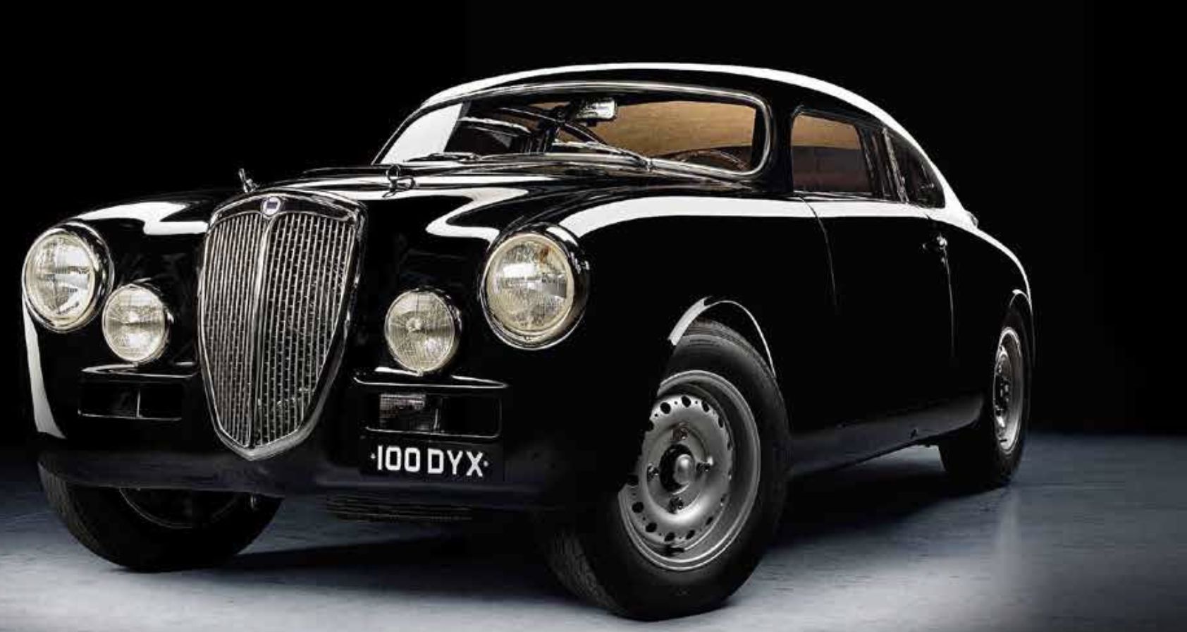 Una classica auto d'epoca nera con dettagli cromati e fari rotondi è raffigurata su uno sfondo scuro. La targa recita "100 DYX". L'auto ha una carrozzeria elegante e lucida e uno stile retrò.