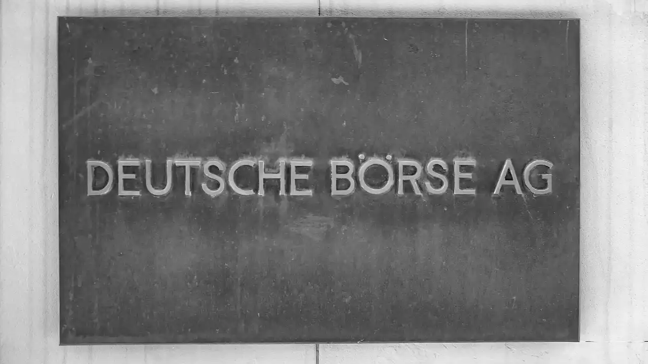 Una targa metallica con il testo inciso "DEUTSCHE BÖRSE AG" montata su una parete chiara.