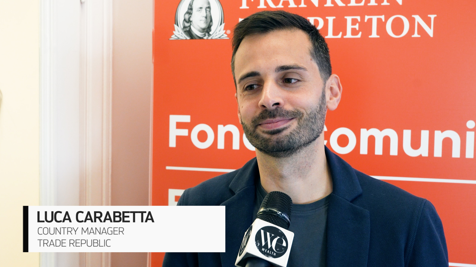 Un uomo con un microfono viene intervistato davanti a uno sfondo rosso di Franklin Templeton. Una didascalia lo identifica come Luca Carabetta, Country Manager di Trade Republic.