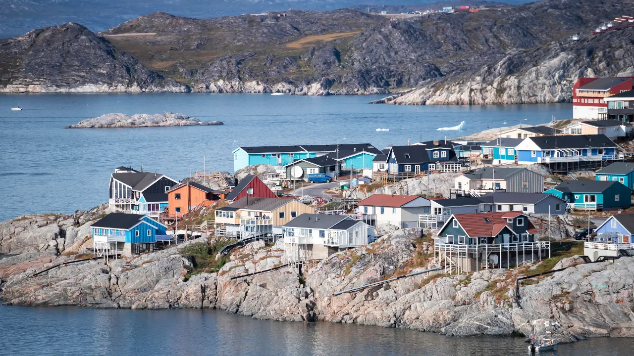 Le case colorate sono sparse su un terreno roccioso vicino all'acqua, con le montagne sullo sfondo e il mare blu e calmo che circonda il villaggio costiero.