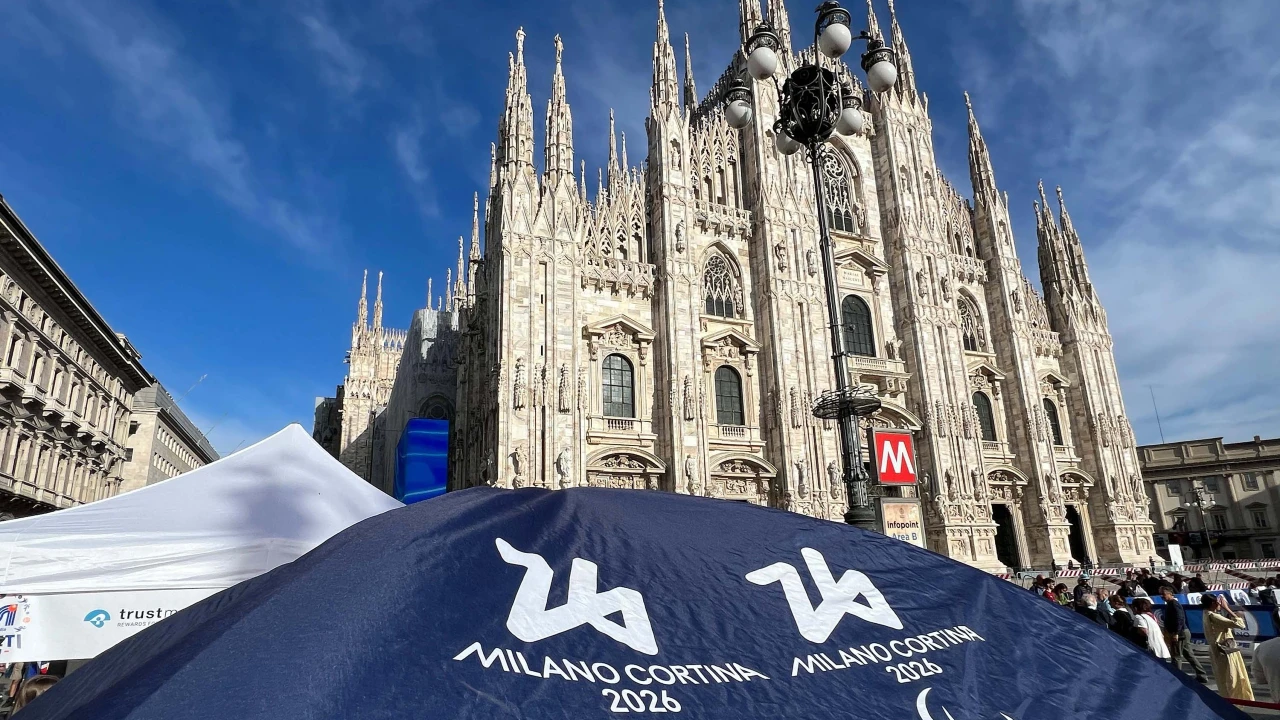 Un grande ombrello milano-cortina con i loghi "Milano Cortina 2026" e Olimpiadi invernali si trova davanti al Duomo di Milano.