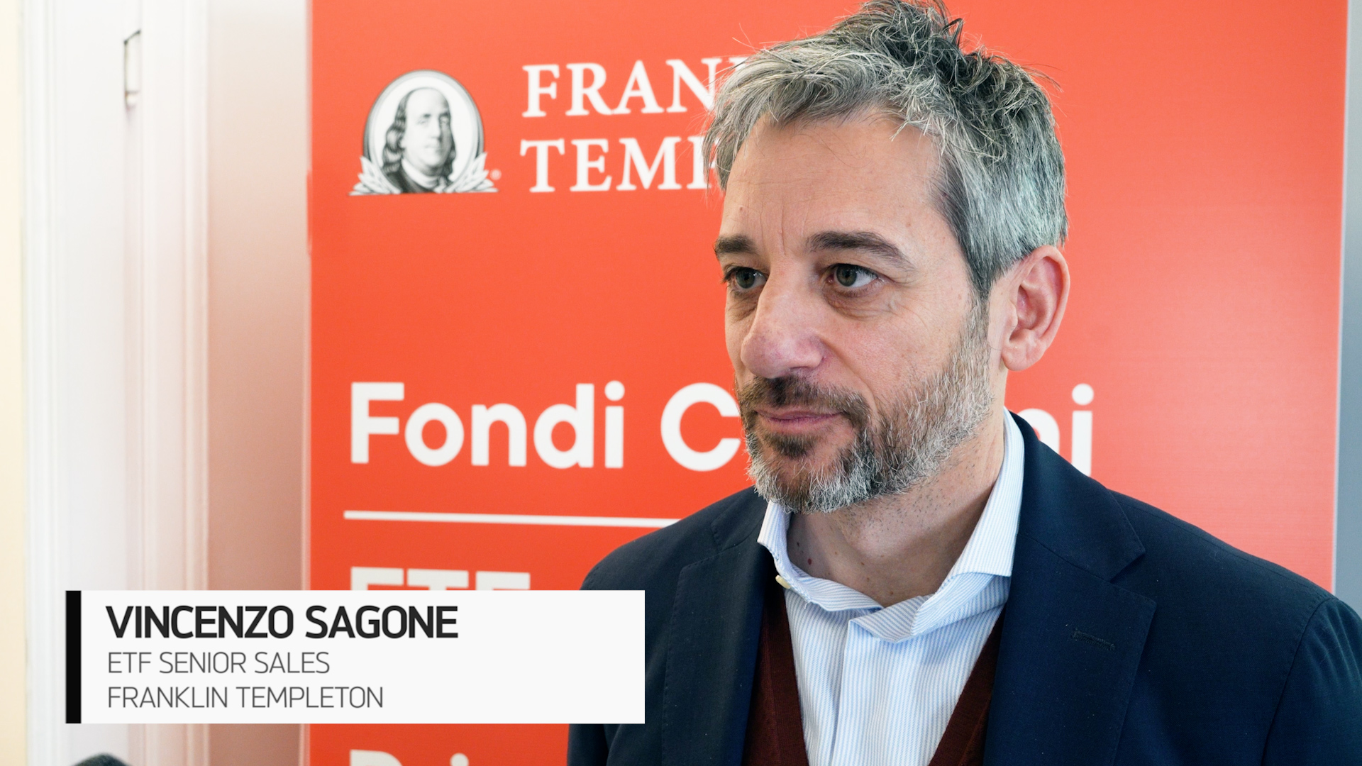 Un uomo con capelli e barba grigi, che indossa un blazer blu e una camicia bianca, è in piedi davanti a un display rosso di Franklin Templeton. Un testo in sovrimpressione recita "Vincenzo Sagone, ETF Senior Sales, Franklin Templeton.