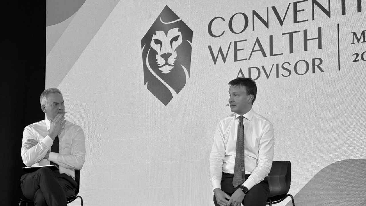 Due uomini in camicia e cravatta siedono sul palco, impegnati in una discussione, davanti a un grande fondale con il logo di un leone e la scritta "CONVEGNO WEALTH ADVISOR BANCA GENERALI".